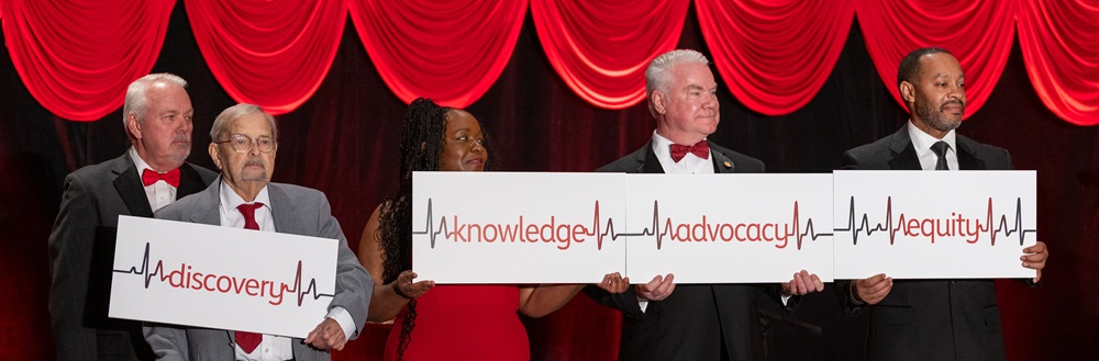 Photo of five people holding up a banner reading equity, knowledge, discovery, and advocacy with each word separated by an EKG reading.